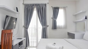 A modern hotel room with a bed, a TV on a stand, a desk, and curtains. - Nice and Comfy Studio Apartment at Signature Park Grande (Jakarta)