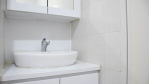 A white bathroom with a sink, a mirror above it, and white tiled walls. - Nice and Comfy Studio Apartment at Signature Park Grande (Jakarta)
