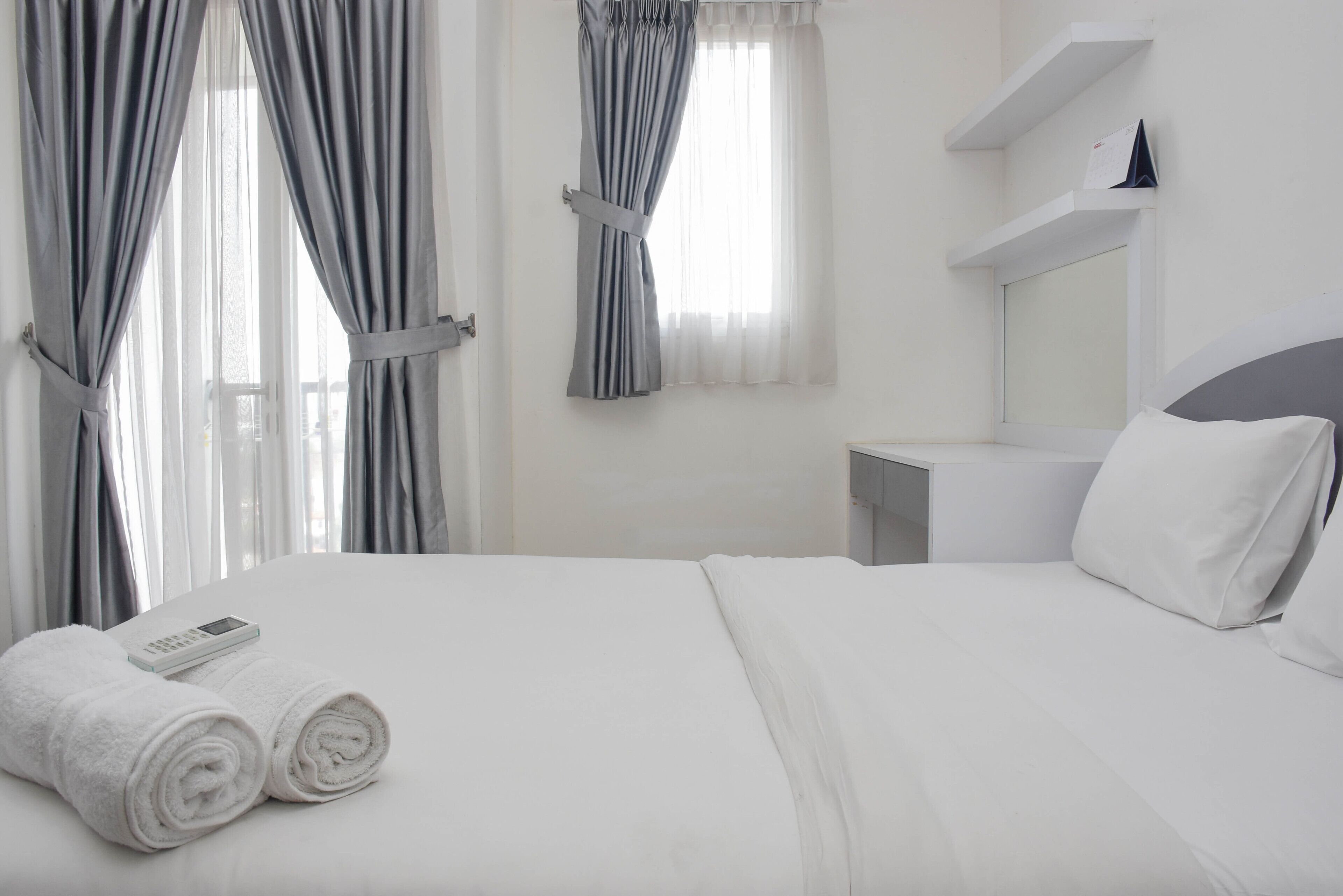 Habitación de hotel con una cama bien hecha, una mesita de noche con lámpara y una ventana con cortinas.