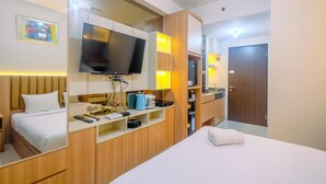 A hotel room with a bed, a TV, a desk with a kettle, and a wardrobe. - Homey and Stylish Studio Room at Transpark Cibubur Apartment (Depok)