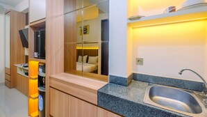 A modern kitchen with a granite countertop, stainless steel sink, and wooden cabinets. - Homey and Stylish Studio Room at Transpark Cibubur Apartment (Depok)