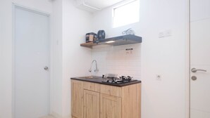 A compact kitchen with wooden cabinets, a black countertop, a gas stove, and a coffee maker on a shelf. - Best Choice and Comfy 3BR at Bassura City Apartment (Jakarta)