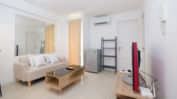 A modern living room with a sofa, coffee table, TV, and a refrigerator. - Best Choice and Comfy 3BR at Bassura City Apartment (Jakarta)