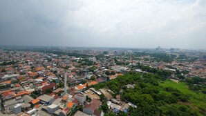 An aerial view of a densely populated urban area with a mix of residential and commercial buildings, a prominent tower, and surrounding greenery. - Best Choice and Comfy 3BR at Bassura City Apartment (Jakarta)