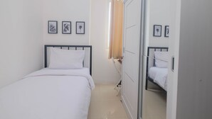 A bedroom with a single bed, a wardrobe, and a mirror. There are three framed pictures on the wall. - Best Choice and Comfy 3BR at Bassura City Apartment (Jakarta)