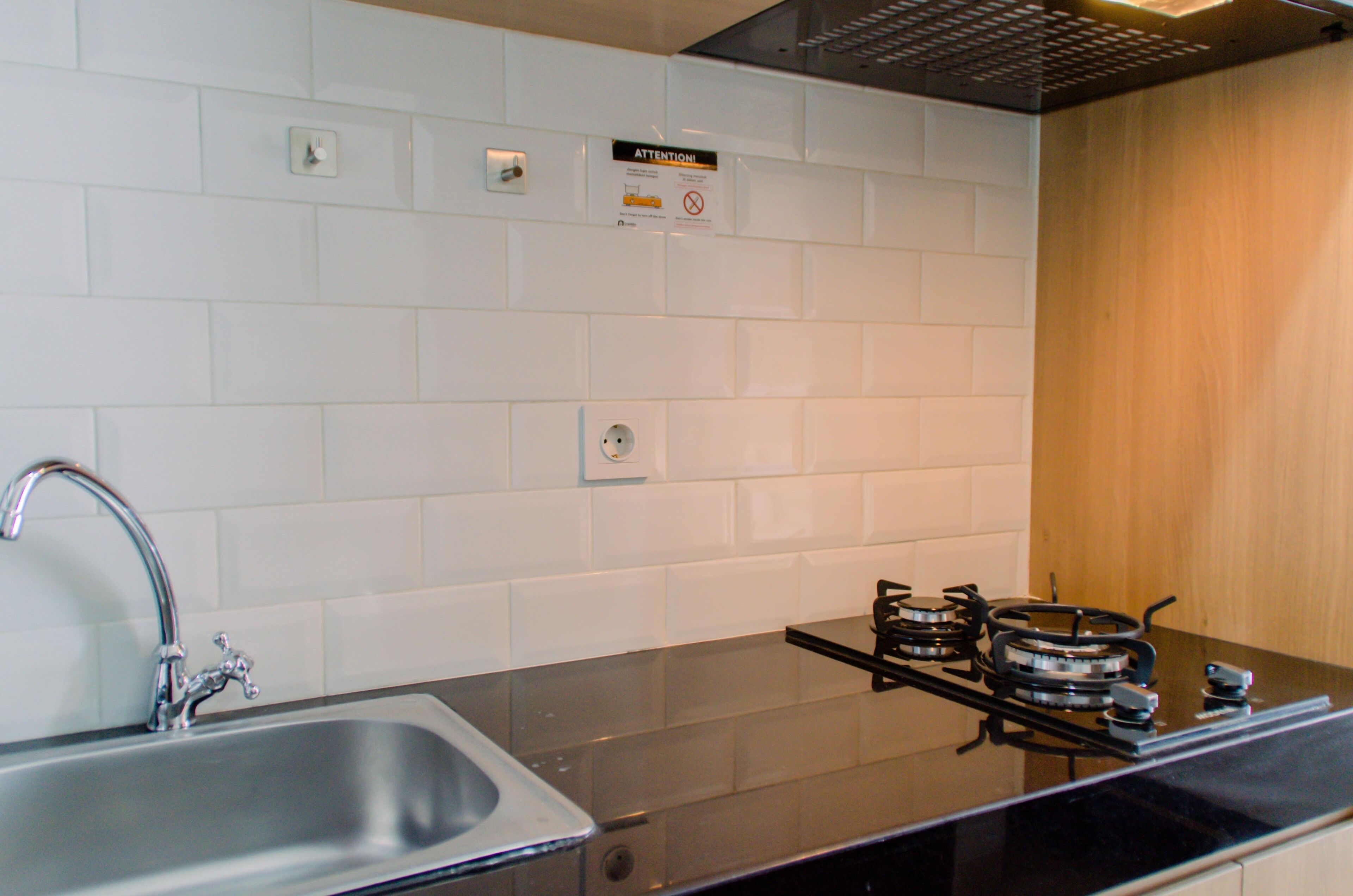 Una cocina moderna con un lavamanos de acero inoxidable, una estufa a gas y paredes cubiertas de azulejos blancos.