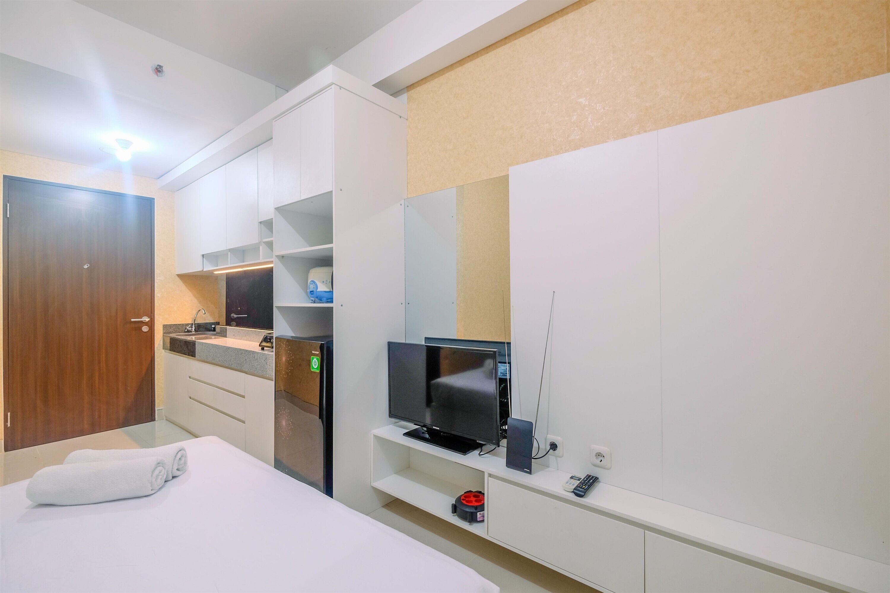 A modern hotel room with a bed, a TV, a small desk, and a kitchenette.