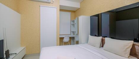 Una habitación de hotel con cama, escritorio, computadora, silla y televisor.
