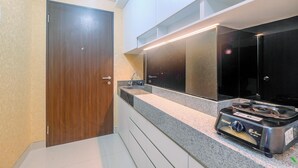 A modern bathroom with a wooden door, a sink with a mirror, and a gas stove. - Homey and Comfort Living Studio Apartment Transpark Cibubur (Depok)