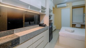 A modern hotel room with a kitchenette, a bed with a rolled towel, and a large mirror. - Homey and Comfort Living Studio Apartment Transpark Cibubur (Depok)