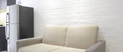 A modern kitchen with a white brick wall, a beige sofa, and a dark-colored refrigerator.