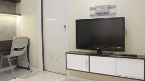 Une chambre moderne avec un téléviseur à écran plat posé sur un meuble, une chaise blanche et une porte dotée d’une poignée.