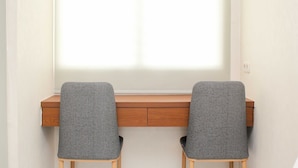 A desk with two grey chairs and a window with blinds. - Nice and Elegant Studio at Riverview Jababeka Apartment (Cikarang)