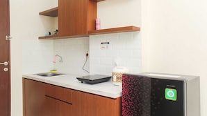 A kitchen with wooden cabinets, a white countertop, a sink, a dish rack, a coffee maker, and a dishwasher. - Nice and Elegant Studio at Riverview Jababeka Apartment (Cikarang)