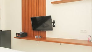 A modern room with a mounted TV, wooden panel wall, and a shelf with a box and a small item. - Nice and Elegant Studio at Riverview Jababeka Apartment (Cikarang)