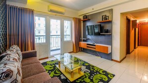 A living room with a sofa, a glass coffee table, and a TV on a wooden stand. - Posh 3BR Residence at Grand Palace Kemayoran (Jakarta)