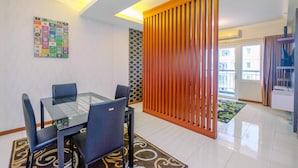 A modern dining area with a glass table and chairs, a decorative wall with a calendar, and a sliding wooden partition. - Posh 3BR Residence at Grand Palace Kemayoran (Jakarta)