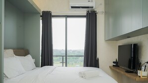 A hotel room with a bed, a TV, and a window with curtains. - Stunning Studio Apartment at Sky House BSD (Pagedangan)