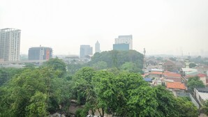 A cityscape with dense greenery in the foreground, a mix of modern and older buildings, and a hazy sky. - Nice and Comfy 1BR Apartment at MT Haryono Residence (Jakarta)