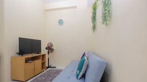 A living room with a grey sofa, a wooden TV stand, a clock on the wall, and a small plant. - Nice and Comfy 1BR Apartment at MT Haryono Residence (Jakarta)