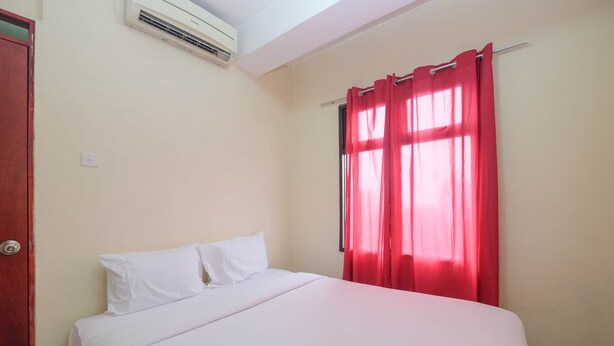 A hotel room with a bed, white bedding, red curtains, and an air conditioning unit on the wall. - Nice and Comfy 1BR Apartment at MT Haryono Residence (Jakarta)