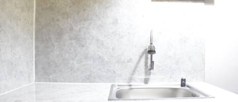 A kitchen with a stainless steel sink, white marble countertops, and a wall-mounted light fixture.