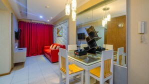 A modern living room with a red sofa, a glass dining table with white chairs, and a large mirror reflecting the room. - Lush 3BR Residence at Grand Palace Kemayoran (Jakarta)