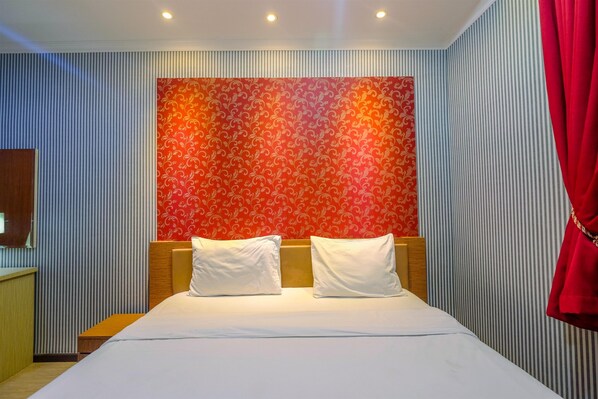 Ein Hotelzimmer mit einem Bett, zwei Kissen, einem hölzernen Kopfteil und einer roten Wand mit Muster.
