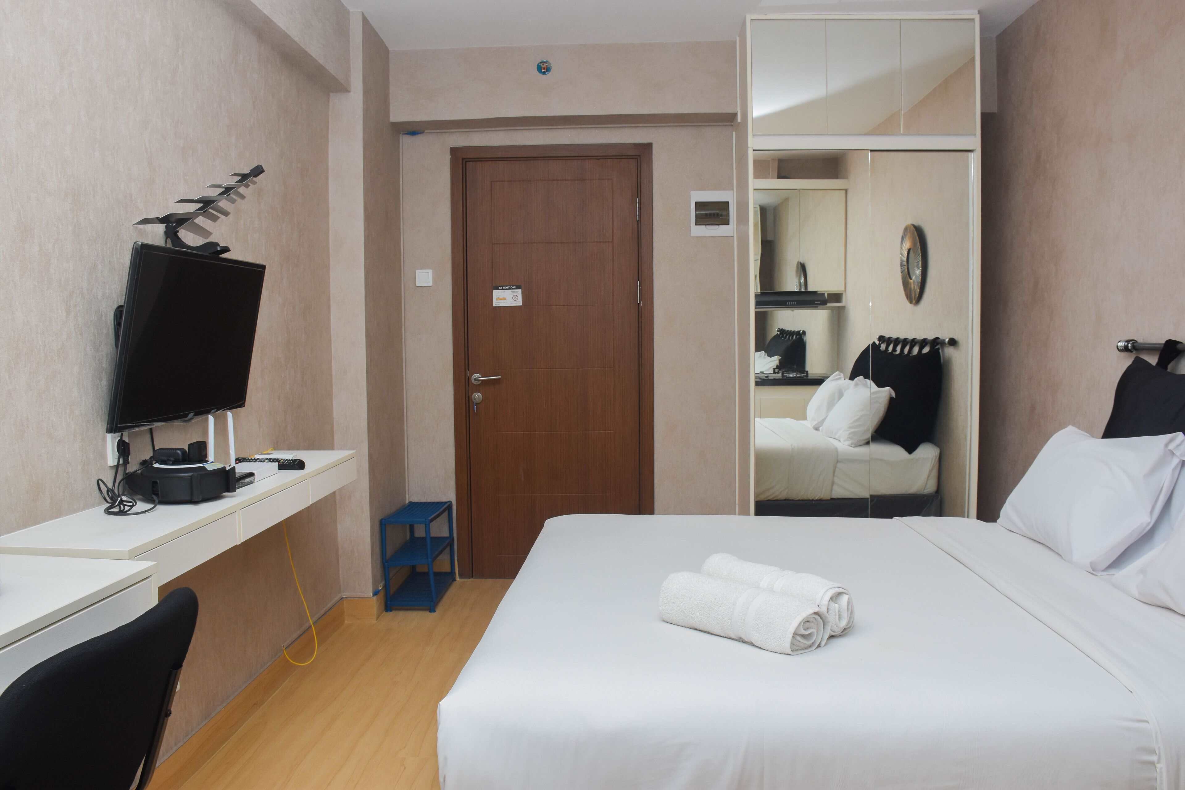 Ein Hotelzimmer mit einem Bett, einem Schreibtisch mit Computer, einem Fernseher und einem Spiegel.