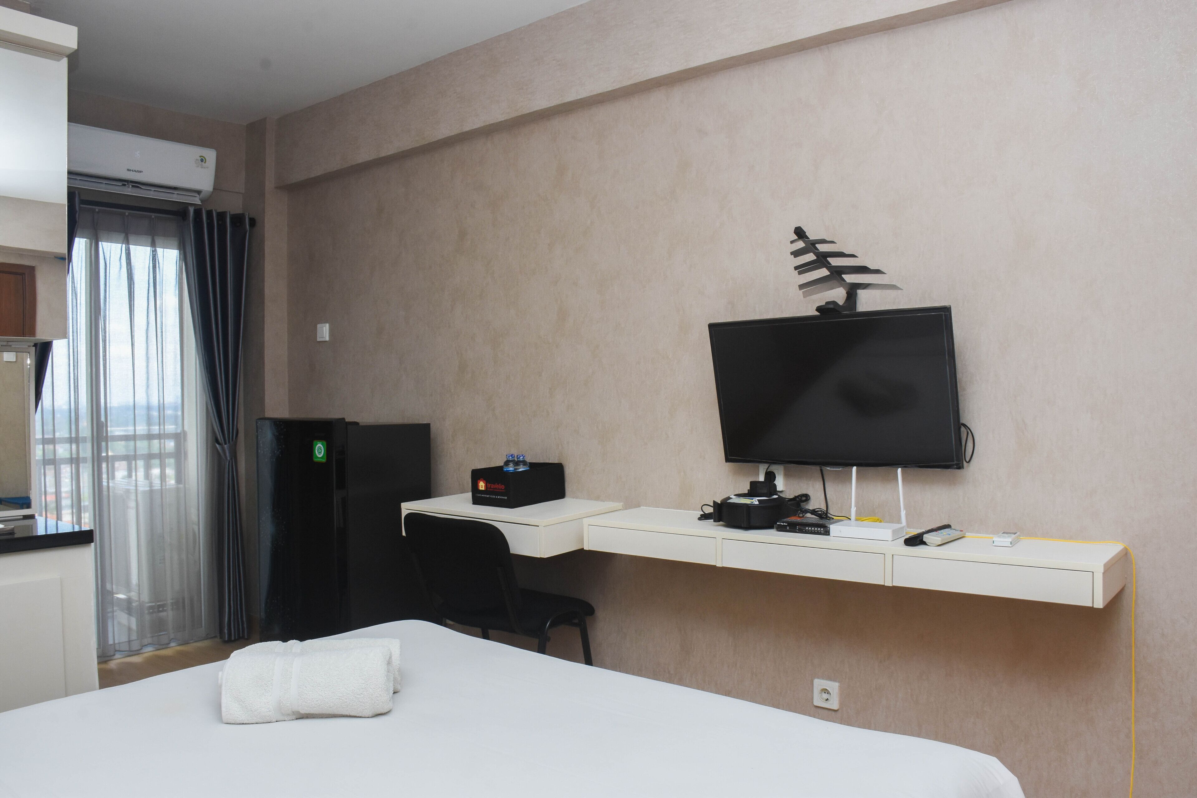 A hotel room with a bed, a desk with a computer, a TV, and a minibar.