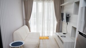 A modern hotel room with a bed, a small round table, a TV, and a built-in kitchen area.