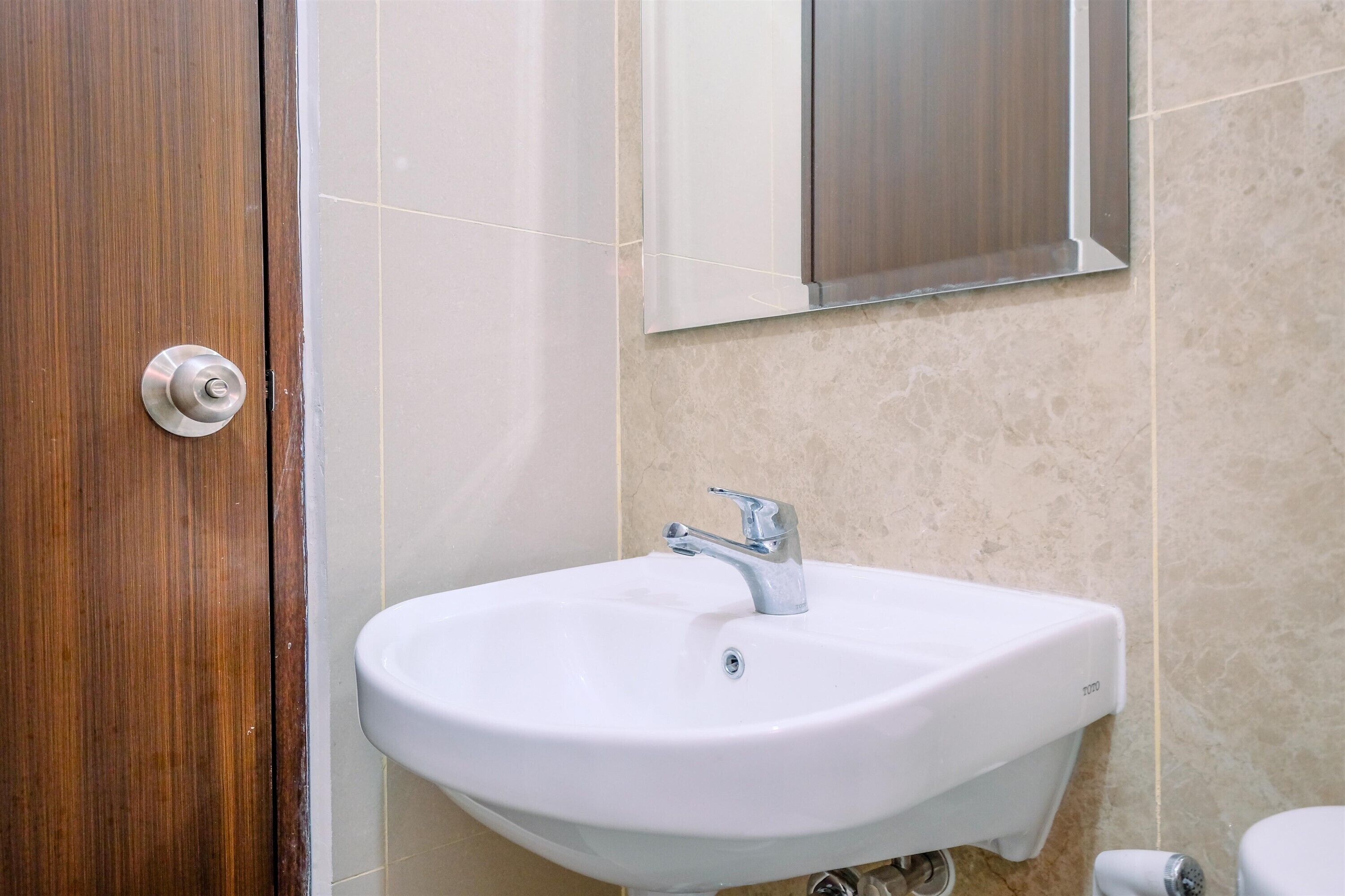 Une salle de bain avec un lavabo blanc, une porte en bois et un miroir.