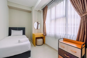 Une chambre d’hôtel comprenant un lit, une table de chevet avec un miroir, une petite table en bois, un petit pouf et une commode avec des tiroirs.