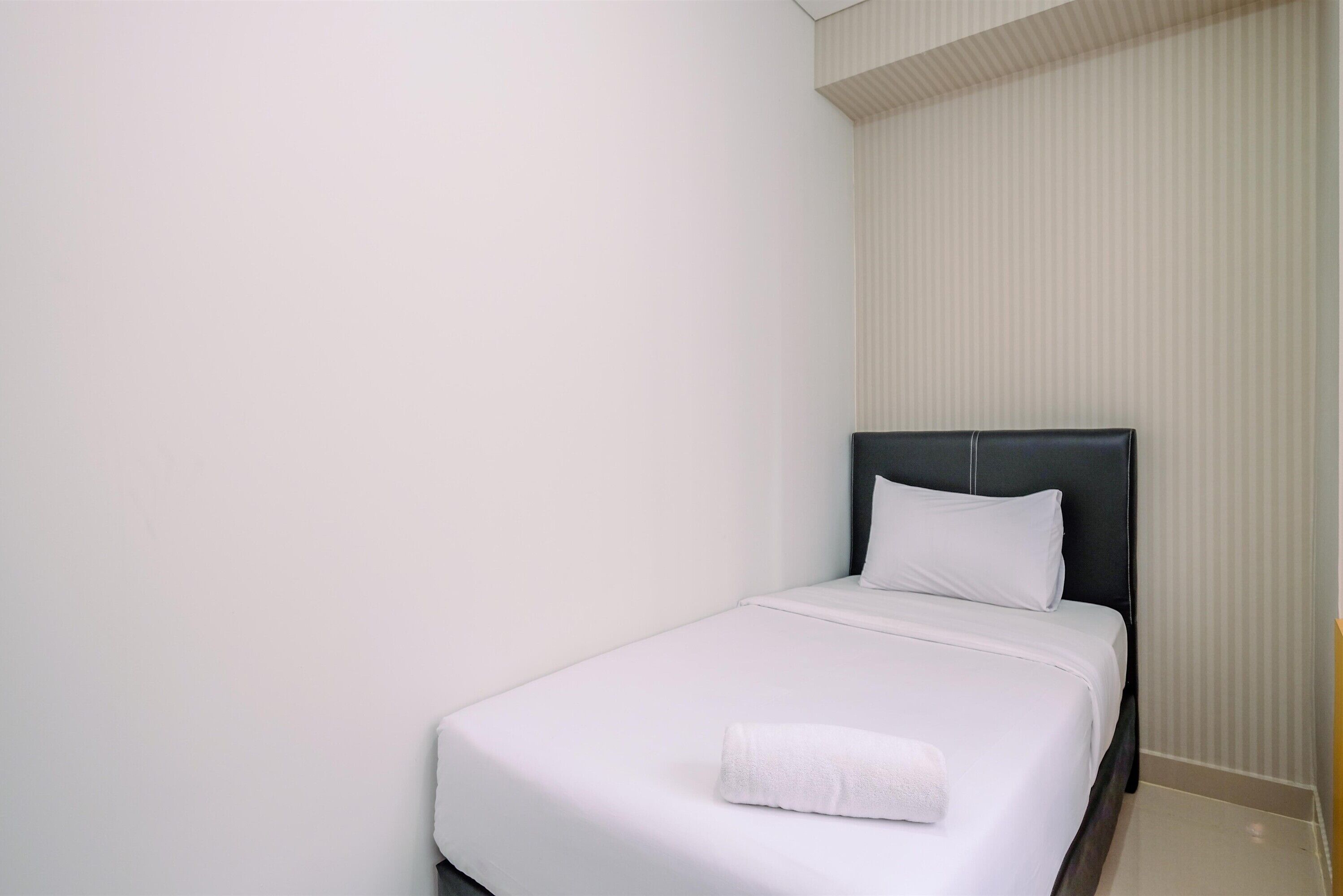 A single bed with white bedding and a dark headboard in a room with plain walls and a striped wallpaper pattern.