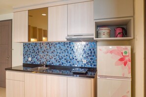 Una cocina con cubierta negra, un lavamanos, una campana extractora de acero inoxidable, un microondas, un tostador y un refrigerador con diseño floral.