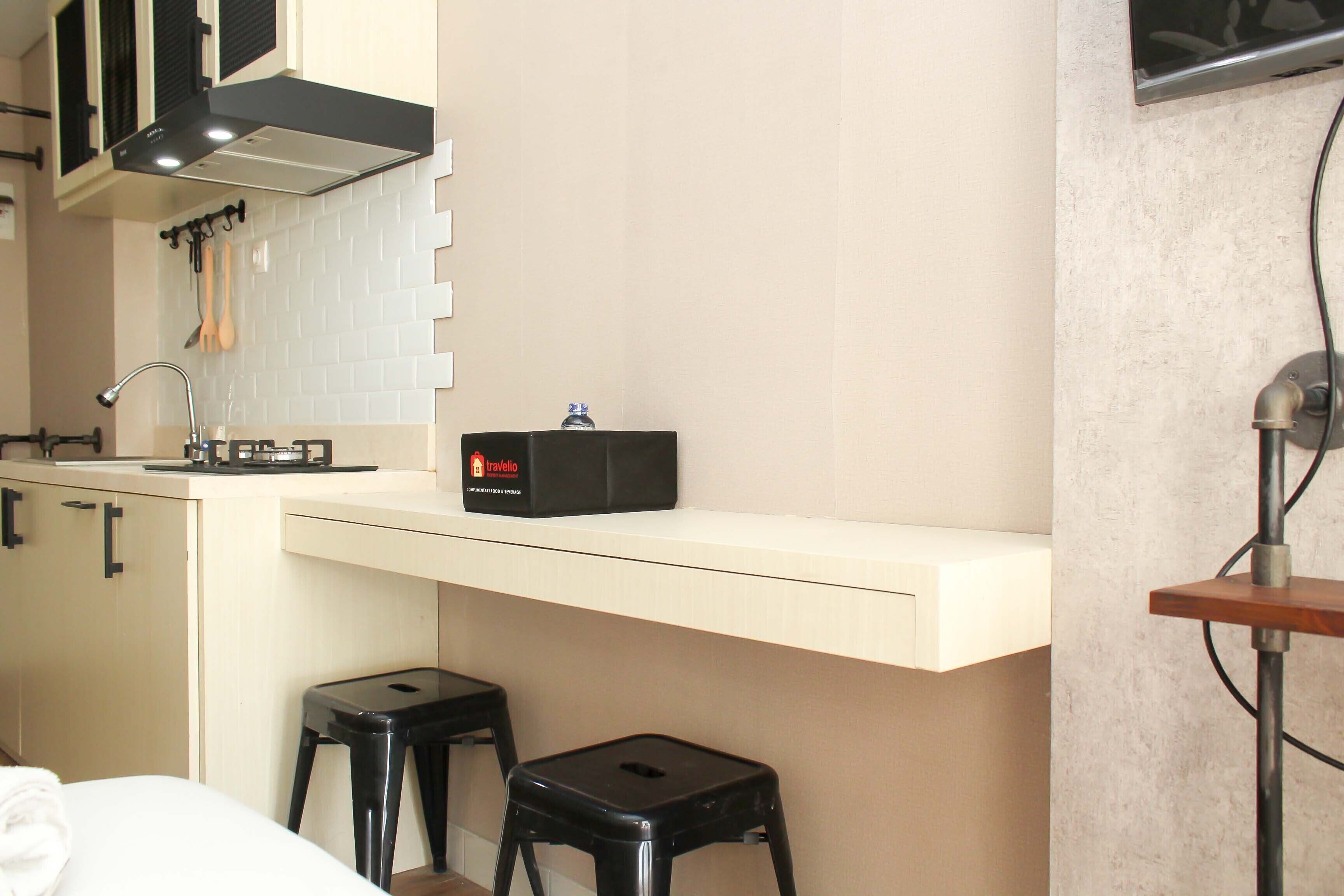 Cocina compacta con encimera, lavamanos y dispensador de agua. Hay dos taburetes negros y una encimera blanca debajo.