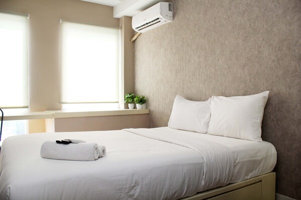 A neatly made bed with white linens, a rolled towel, and a remote control on the left side. - New and Cozy Studio at Patraland Urbano Apartment (Bekasi)
