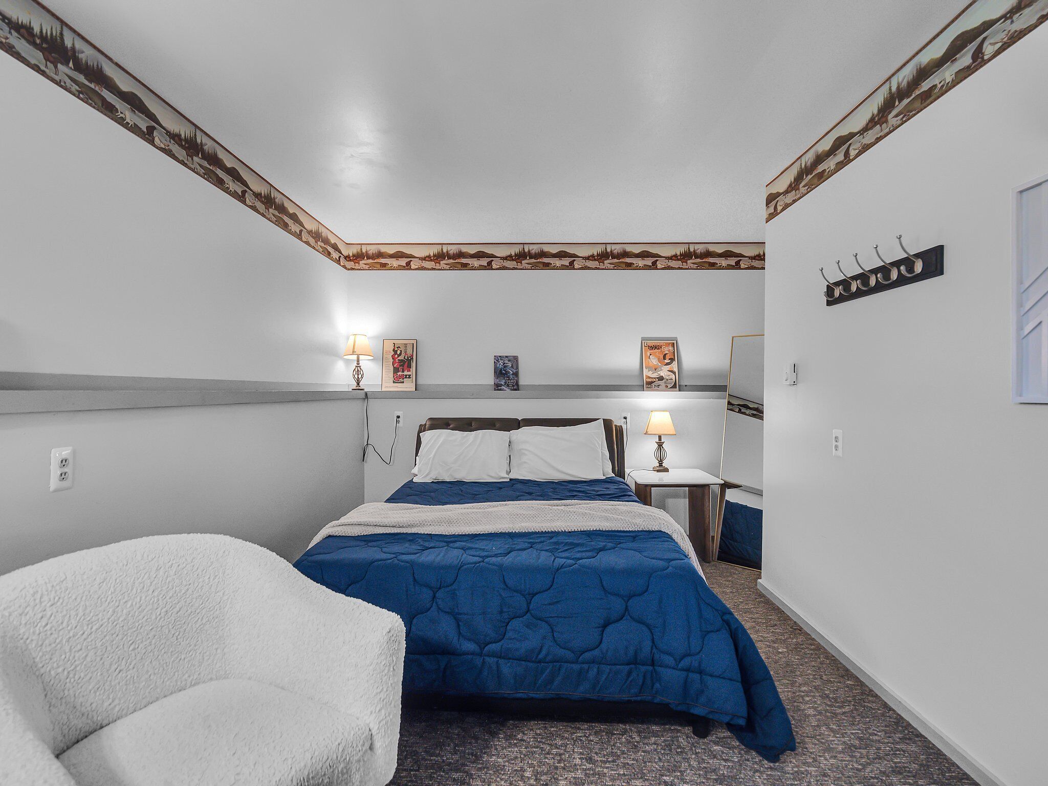 Un dormitorio con cama, una silla, una mesita de noche, una lámpara y decoración en la pared.