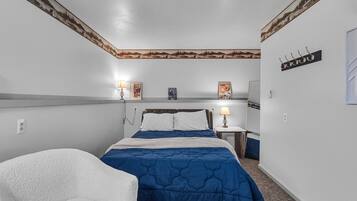 Un dormitorio con cama, una silla, una mesita de noche, una lámpara y decoración en la pared.