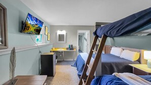 A hotel room with bunk beds, a desk with a computer, a mirror, and a TV on the wall.