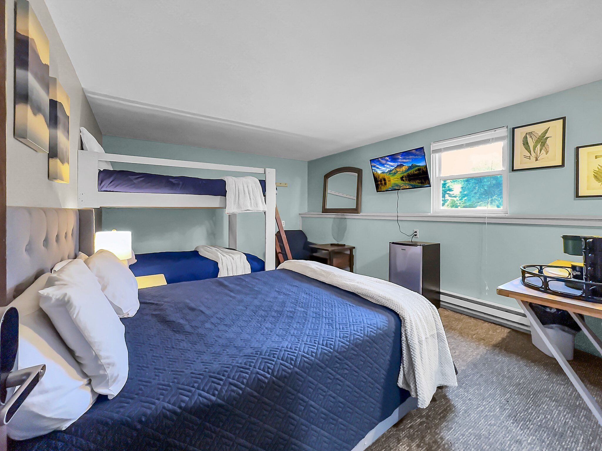 Ein Schlafzimmer mit Etagenbett, Schreibtisch, Computer, Fernseher und gerahmten Bildern an der Wand.