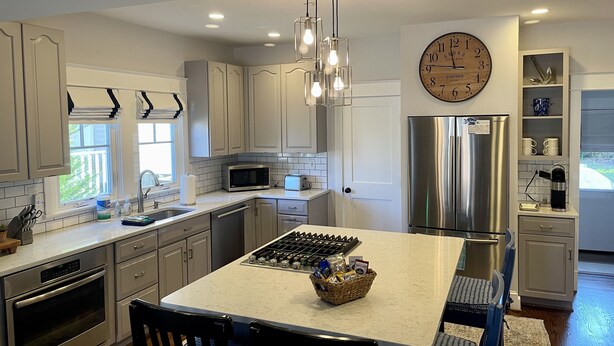 A modern kitchen with white cabinets, stainless steel appliances, a central island, and a large wall clock. - Recently Renovated Annapolis Home - Conveniently Located (Annapolis)