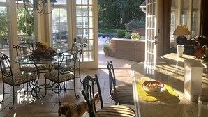 Un coin repas avec une table en verre, des chaises en métal et un lustre. De grandes fenêtres offrent une vue sur un jardin.