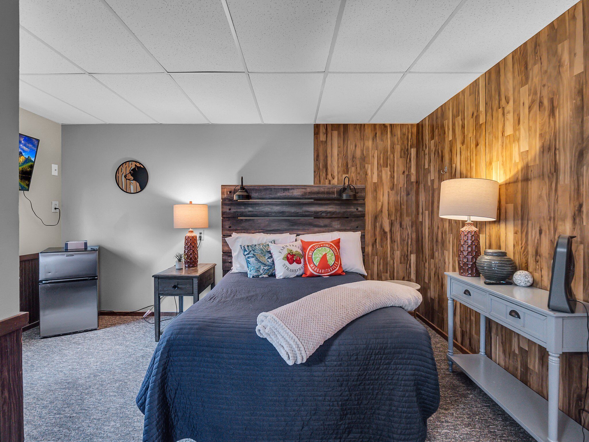 A bedroom with a bed, nightstands, a wooden accent wall, and a TV on the wall.