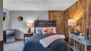 A bedroom with a bed, nightstands, a wooden accent wall, and a TV on the wall.