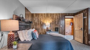 A bedroom with a bed, bedside tables, a lamp, a fan, and a wooden wall panel. - Timberline Lodge - Downtown Ellicottville - Room 200 (Ellicottville)