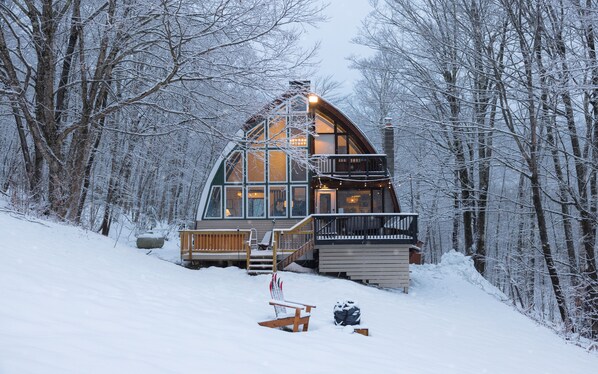 A cabin with a large window, a balcony, and a wooden deck.