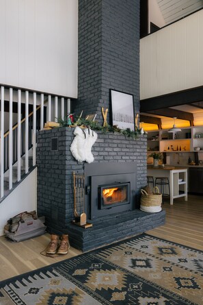 A modern living room with a fireplace, a staircase, and a kitchen area.