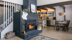 A modern kitchen with a fireplace, wooden flooring, and a dining area with chairs and a table.