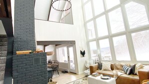 A spacious living room with a high ceiling, a fireplace, a large window, and a cozy seating area.